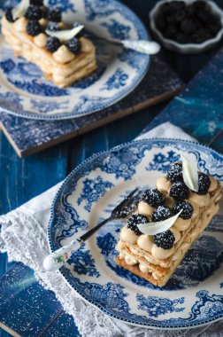 Fransız Pasta krema ve böğürtlen ahşap masa üzerinde mavi plaka ile