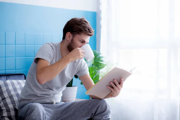 Giovane lettura libro e bere caffè sul divano nel soggiorno — Foto Stock