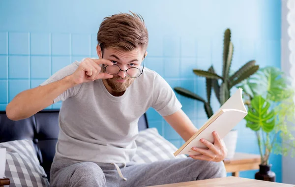 Giovane uomo indossare occhiali libro di lettura sul divano in salotto — Foto Stock