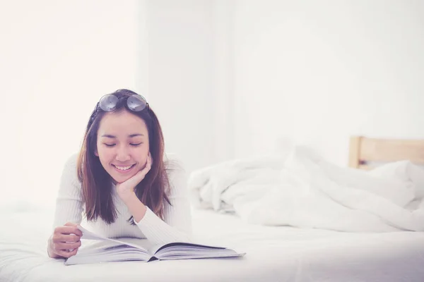 Mujer encantadora acostada en la cama leyendo un libro en el dormitorio . —  Fotos de Stock