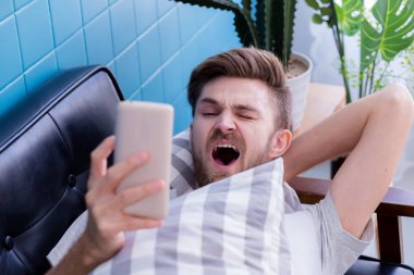 amerikalı adam bir akıllı telefon medya içeriği izlerken ve esneme