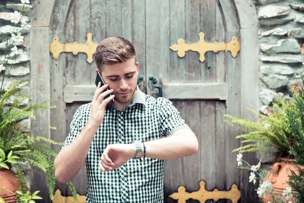 Hombre de pie en el jardín mirando el reloj de mano y hablando de teléfono  - —  Fotos de Stock