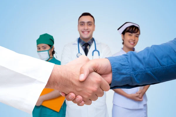 Los jóvenes médicos apretón de manos en el consultorio con el equipo médico de vuelta —  Fotos de Stock