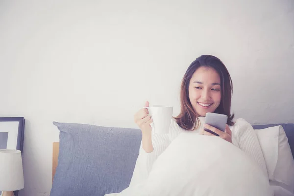 Wesoły młody Asian kobieta siedzący w łóżko z smartphone i dr — Zdjęcie stockowe