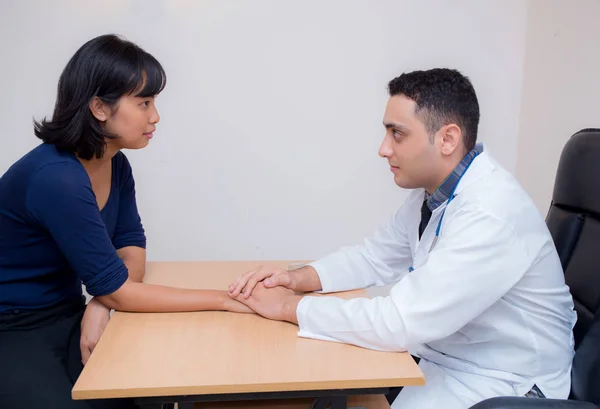 Amichevole medico di sesso maschile mano tenendo mano paziente seduto al de — Foto Stock