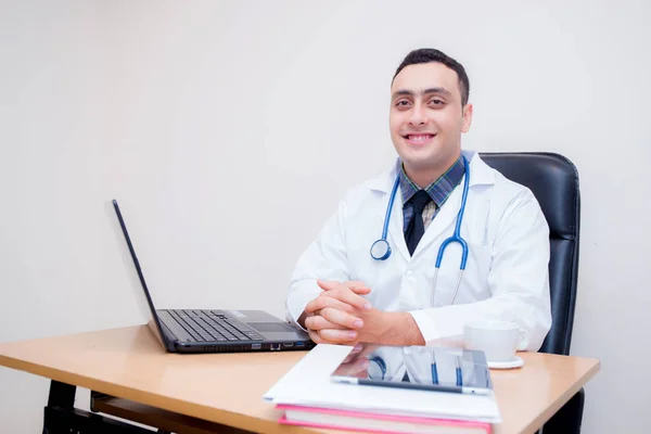 Confiado médico varón sentado en el escritorio de la oficina y sonriendo, médico —  Fotos de Stock