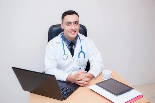 Confiado médico varón sentado en el escritorio de la oficina y sonriendo, médico — Foto de Stock
