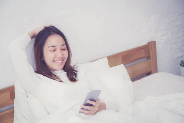 Kobieta Asian model trzyma telefon komórkowy z obudzić w sypialni — Zdjęcie stockowe