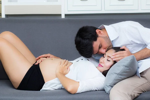 Mąż całuje czoło żony z ciężarnym brzuchu podczas si — Zdjęcie stockowe