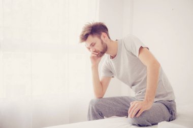 Amerikalı adam esniyor. Adam bir yatakta oturan ciddi ve sorun c