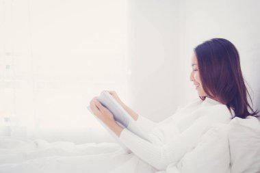 Asyalı kadın bir kitap okuma ve yatak odasında gülümseyen. yaşam tarzı con