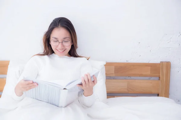 Mujer asiática leyendo un libro y sonriendo en el dormitorio. estilo de vida con —  Fotos de Stock