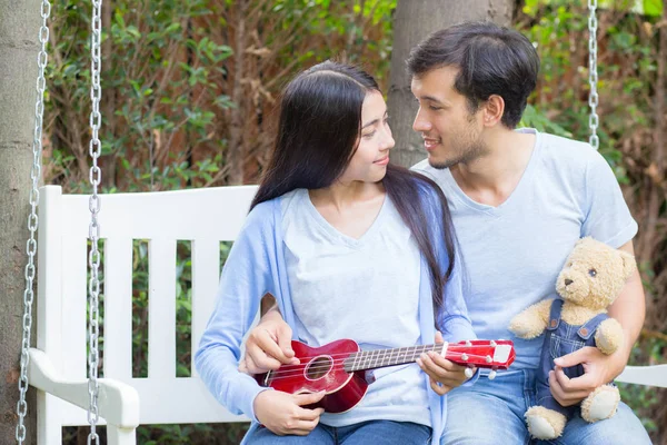 Joven asiática mujer y hombre pareja sentado en parque jugando ukelele — Foto de Stock