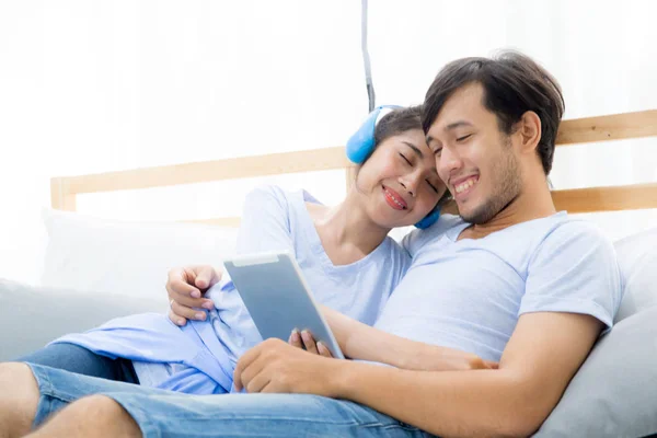 Beautiful asian young couple listening to music with tablet on b