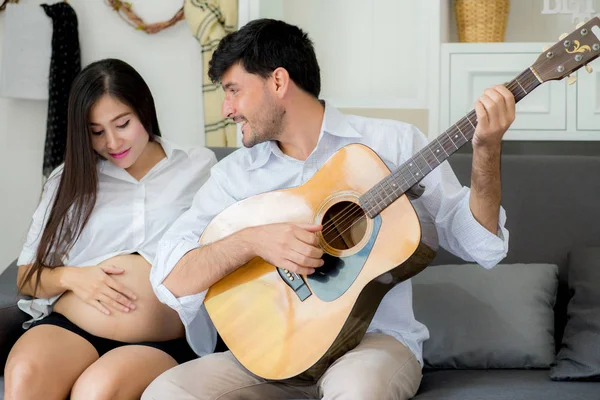 Man spelar gitarr och vacker gravid mamma i Living — Stockfoto