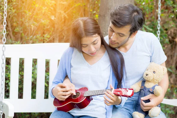 Jovem mulher asiática e homem casal sentado no parque jogar ukulele — Fotografia de Stock