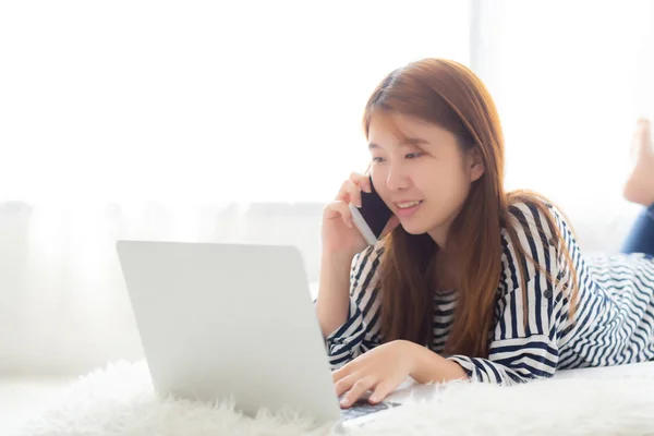 Hermosa mujer joven asiática acostada en la cama usando el ordenador portátil y hablando —  Fotos de Stock