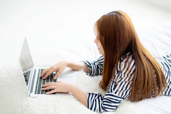 Hermosa mujer joven asiática acostada en la cama usando el ordenador portátil en el dormitorio — Foto de Stock