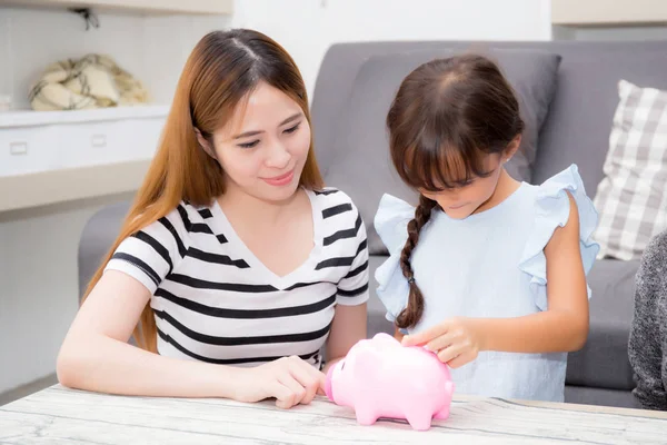 Asian mother and daughter putting coin in piggy bank, mom and ki