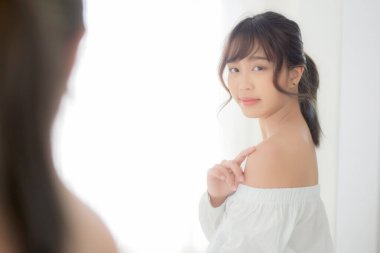 Güzel, genç Asyalı kadın elbiselerini denerken gülümsüyor.