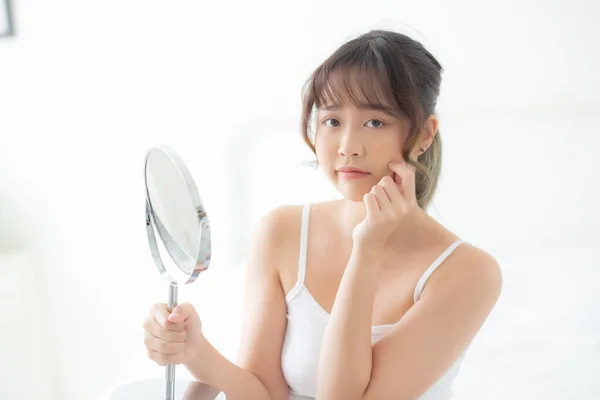 Krásná mladá asijská žena se dívá do zrcadla s akné problém — Stock fotografie