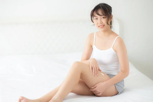 Belle jeune femme asiatique assise sur un lit caressant les jambes avec — Photo