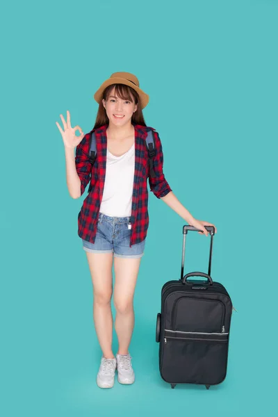Beautiful young asian woman pulling suitcase isolated on blue ba