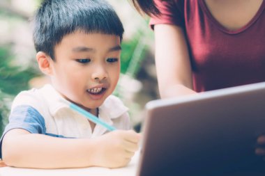 Evlat çalışmak için dijital tablet bilgisayar kullanıyor ve interneti annesiyle birlikte öğreniyor, evden eğitim, aile eğlencesi, anne çocuğa ve ev ödevlerini teknoloji, yaşam tarzı konsepti ile öğretiyor..