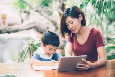 Evlat çalışmak için dijital tablet bilgisayar kullanıyor ve interneti annesiyle birlikte öğreniyor, evden eğitim, aile eğlencesi, anne çocuğa ve ev ödevlerini teknoloji, yaşam tarzı konsepti ile öğretiyor..