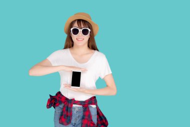 Güzel, genç Asyalı bir kadın yaz tatili seyahatlerinde sunum yapmak için akıllı cep telefonu kullanıyor mavi arka planda izole edilmiş Asyalı bir kız akıllı telefon tutuyor, tatil kavramı..
