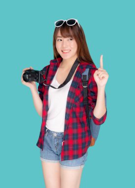 Güzel genç Asyalı bir kadın seyahat gezisi sunuyor. Mavi arka planda izole edilmiş bir şeyi işaret ediyor. Faaliyet hobisi olan bir kız..