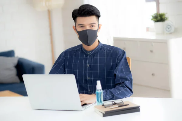 Young business man in face mask working from home with laptop computer on desk for protection for outbreak of covid-19 and healthcare, male quarantine stay home using notebook on desk, new normal.