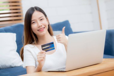 Genç Asyalı kadın internette dizüstü bilgisayarla internetten internet alışverişi yapıyor. Mutlu kız ödemesi kanepe, alışveriş ve ödeme, iş konsepti..