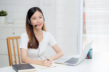 İnternette kulaklık takan genç Asyalı bir kadın. Masasında e-öğrenme, kulaklık takan bir kız. Evde dizüstü bilgisayarla interneti öğrenen bir kız..