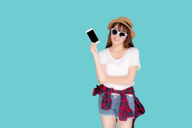 Güzel, genç Asyalı bir kadın yaz tatili seyahatlerinde sunum yapmak için akıllı cep telefonu kullanıyor mavi arka planda izole edilmiş Asyalı bir kız akıllı telefon tutuyor, tatil kavramı..