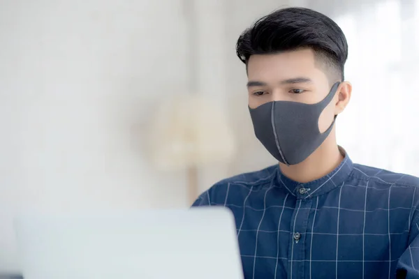 Young business man in face mask working from home with laptop computer on desk for protection for outbreak of covid-19 and healthcare, male quarantine stay home using notebook on desk, new normal.