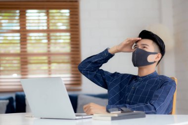 Evde dizüstü bilgisayarla çalışan maskeli genç bir iş adamı ve covid-19 salgını için masabaşında sıkılıyor. Erkek karantina mutsuz, yeni normal bir not defteri kullanarak evde kalıyor..