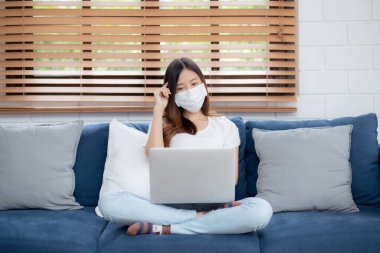 Yüz maskeli Asyalı genç bir iş kadını bilgisayardan internete, oradan oturma odasına, oradan tıbbi maskeli bir kız ve kovid-19 için karantinaya alma fikrini ve çalışmasını düşün..