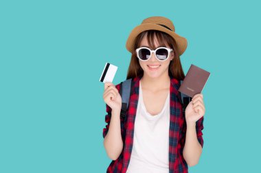 Güzel genç Asyalı kadın şapka takıyor ve güneş gözlüğü takıyor. Yaz seyahatinde kredi kartı ve pasaport gösteriyor. Mavi arka planda izole edilmiş..