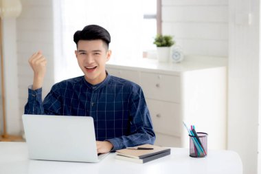 Mutlu genç iş adamı dizüstü bilgisayar işini evde heyecanlı ve başarılı bir şekilde bitiriyor, iş adamı başarıyla ve sürprizle dolu bir not defteri kullanıyor, serbest ya da çalışan, memnun ve memnun..