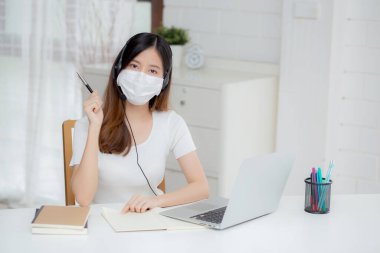 İnternette kulaklık takan genç Asyalı bir kadın. Masasında e-öğrenme, kulaklık takan bir kız. Evde dizüstü bilgisayarla interneti öğrenen bir kız..