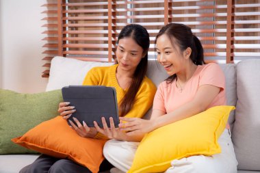 Oturma odasında dijital tablet kullanan iki genç Asyalı kadın, sosyal medyayı internet tableti ve konuşma mesafesi için kullanan kadın, yaşam tarzı kavramı.