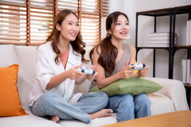 İki Asyalı kadın, evdeki rahat bir oturma odasında bilgisayar oyunu oynuyorlar. Eğlence, arkadaşlık ve neşeli bir yaşam tarzı. Asyalı arkadaşlar, eğlence ve oyun paylaşımının keyfini çıkarıyorlar..