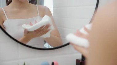 Genç Asyalı kadının aynaya bakan elini sil evdeki banyoda pamuklu havluyla, kişisel bakım, sağlık ve hijyen, ev hayatı, yaşam tarzı ve temizlik..