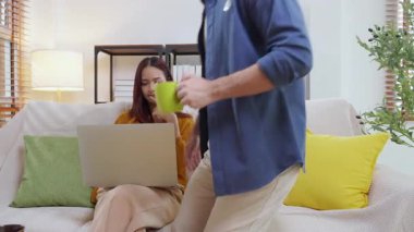 Genç Asyalı çift rahat ve rahat bir şekilde dizüstü bilgisayara bakıyor. Oturma odasındaki kanepede oturuyor. Kanepede dizüstü bilgisayar izliyor..