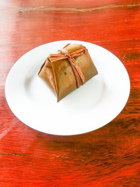 Buharda pişmiş, muz yaprağına sarılmış, ahşap zemine konmuş, beyaz bir tabakta.