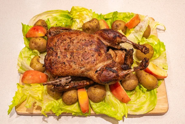 Christmas goose whool roasted and crispy on the cutting board with roasted potatoes, apples and brussels sprouts.
