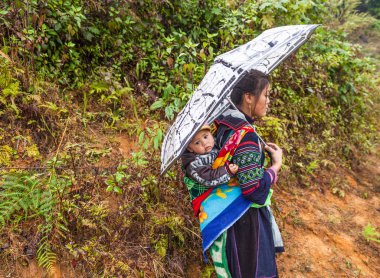 Sa pa, Vietnam-13 Aralık 2013. Bir çocuk sırtında taşıyan Vietnamca siyah Hmong kadın dağ yolu yağmurlu günde köyünün Muong Hoa Valley için 13 Aralık 2013 Sa Pa üzerinde yürüyor