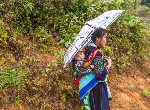Sa pa, Vietnam-13 Aralık 2013. Bir çocuk sırtında taşıyan Vietnamca siyah Hmong kadın dağ yolu yağmurlu günde köyünün Muong Hoa Valley için 13 Aralık 2013 Sa Pa üzerinde yürüyor