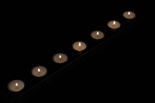 Pequenas velas redondas acesas em um suporte de vela escura em um fundo preto.velas iluminadas — Fotografia de Stock